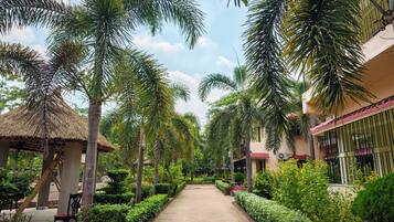 A pathway flanked by palm trees and a building with a red roof.