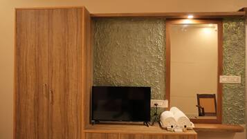 A wooden wardrobe with a flat-screen TV, a mirror, and a small shelf with toiletries.