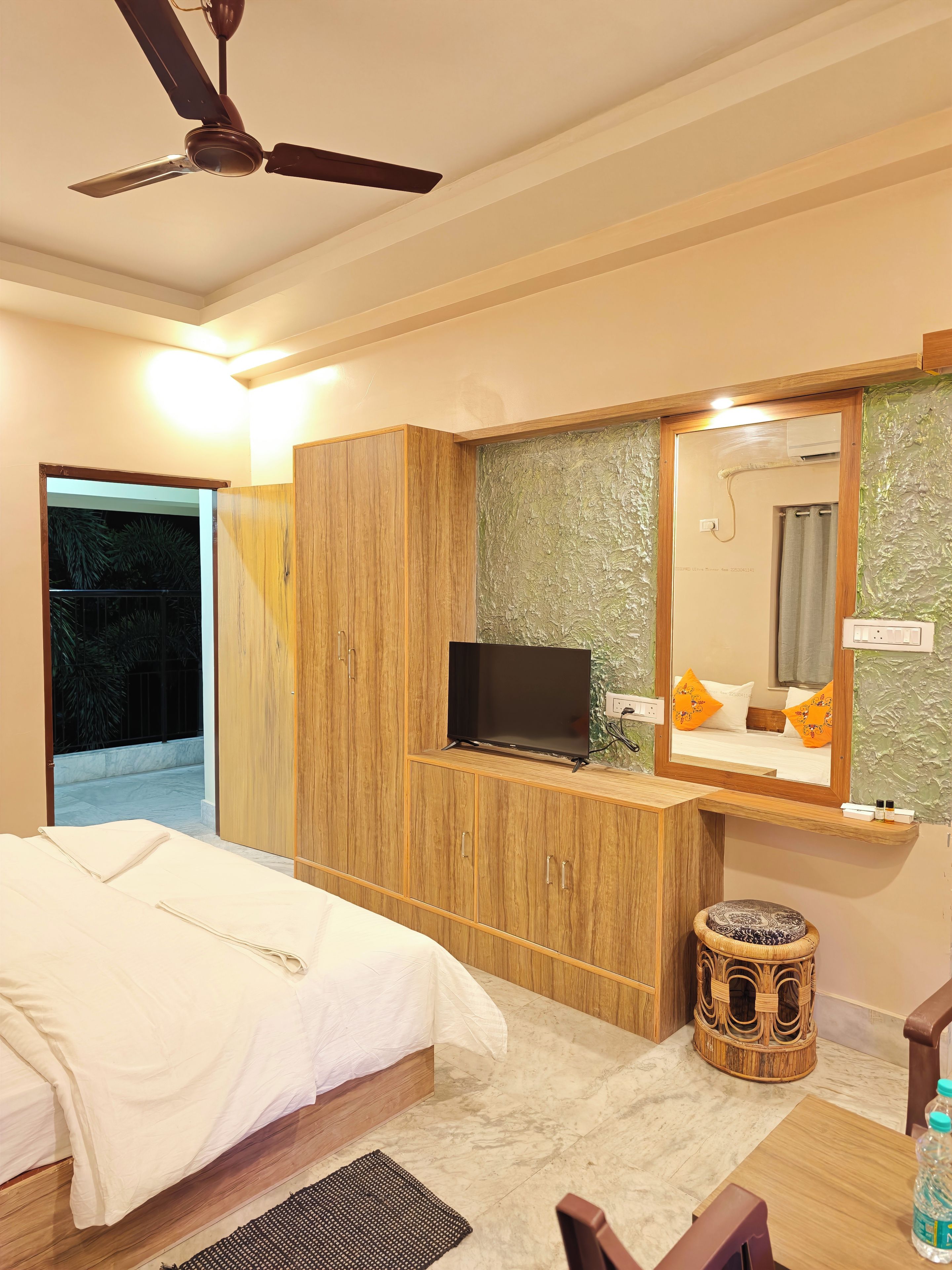 A hotel room with a bed, a television on a wooden cabinet, a bathroom with a mirror, and a ceiling fan.