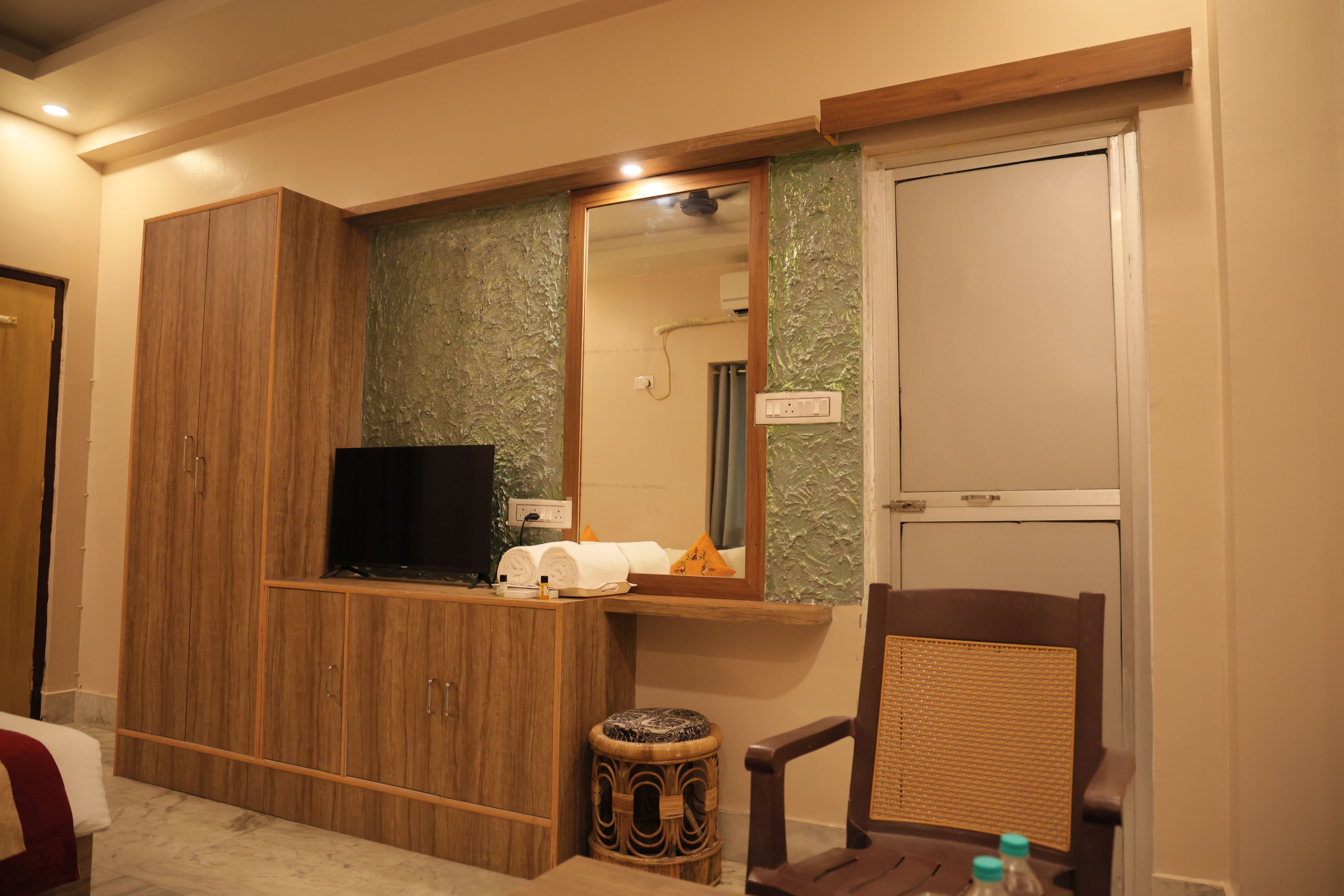 Una habitación de hotel con un armario de madera, un televisor de pantalla plana, un espejo, un taburete pequeño y una silla.