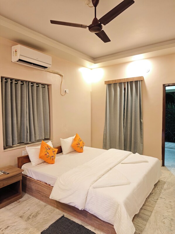 A hotel room with a bed, a ceiling fan, an air conditioning unit, and curtains.
