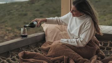 Una persona sirve vino en una copa sobre una terraza de madera con vistas a un paisaje montañoso.