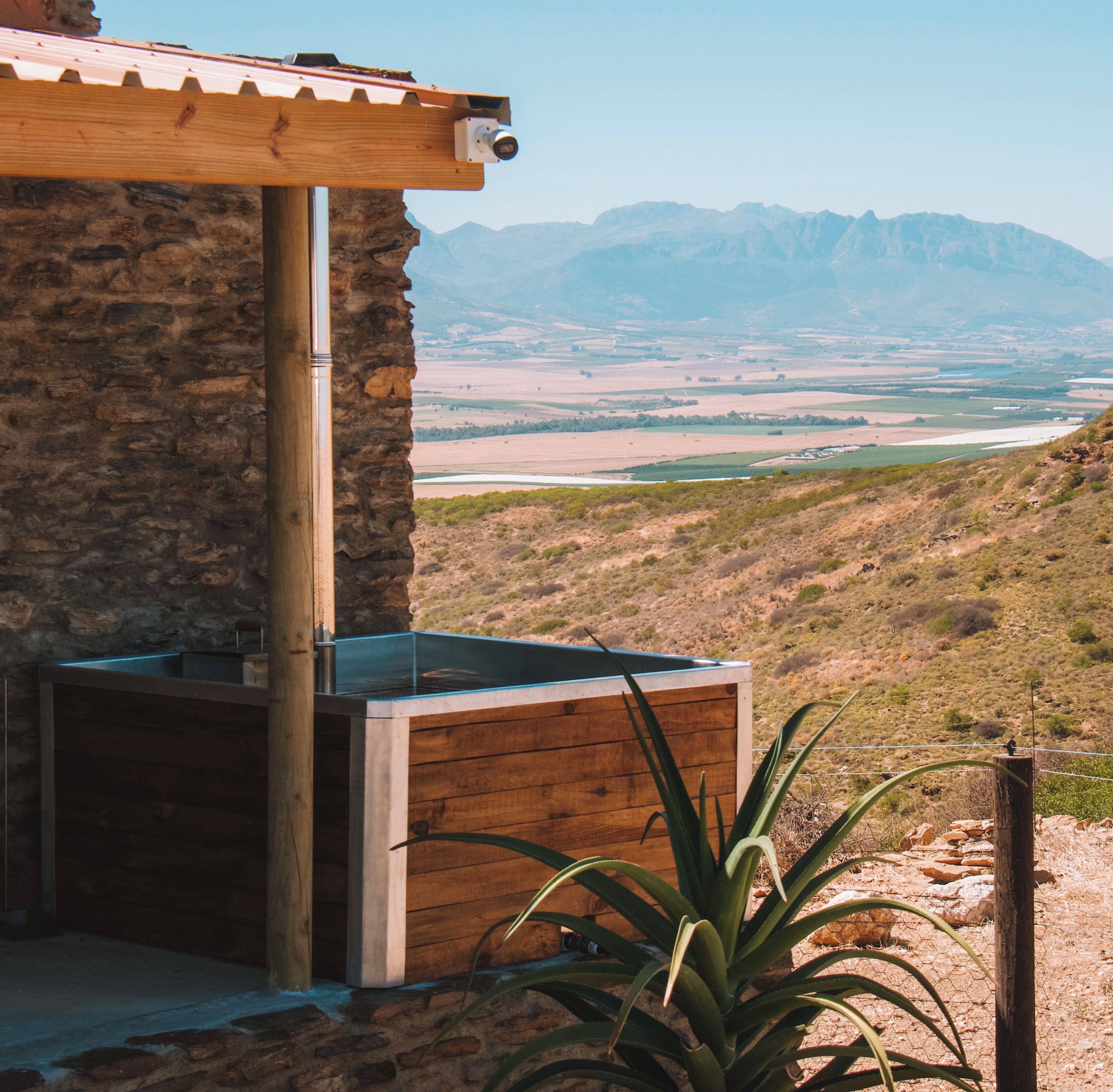 A stone building with a wooden pergola and a view of a valley and mountains.