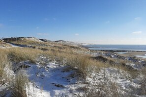 Een kustlandschap met besneeuwde duinen, een heldere lucht en een verre horizon van de zee.
