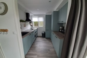 A narrow kitchen with light blue cabinets, a stainless steel range hood, and a window providing natural light. - Holiday apartment with 3 bedrooms (Zoutelande)