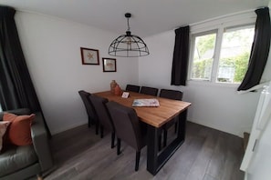 A dining area with a wooden table, black chairs, a hanging light fixture, and a window with curtains. - Holiday apartment with 3 bedrooms (Zoutelande)