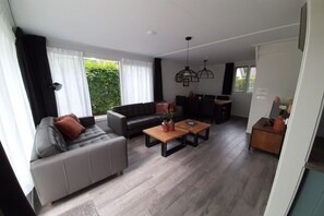 A modern living room with a grey sofa, a wooden coffee table, and a dining area with chairs. - Holiday apartment with 3 bedrooms (Zoutelande)