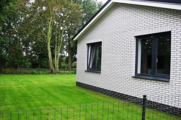 Une maison moderne avec une façade en briques, une pelouse bien entretenue et une clôture en métal.
