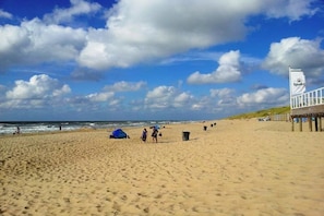Une plage avec une tente, une poubelle et une jetée sur laquelle flotte un drapeau.