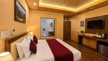 A hotel room with a bed, a television, a desk, and a bathroom visible through a glass door.