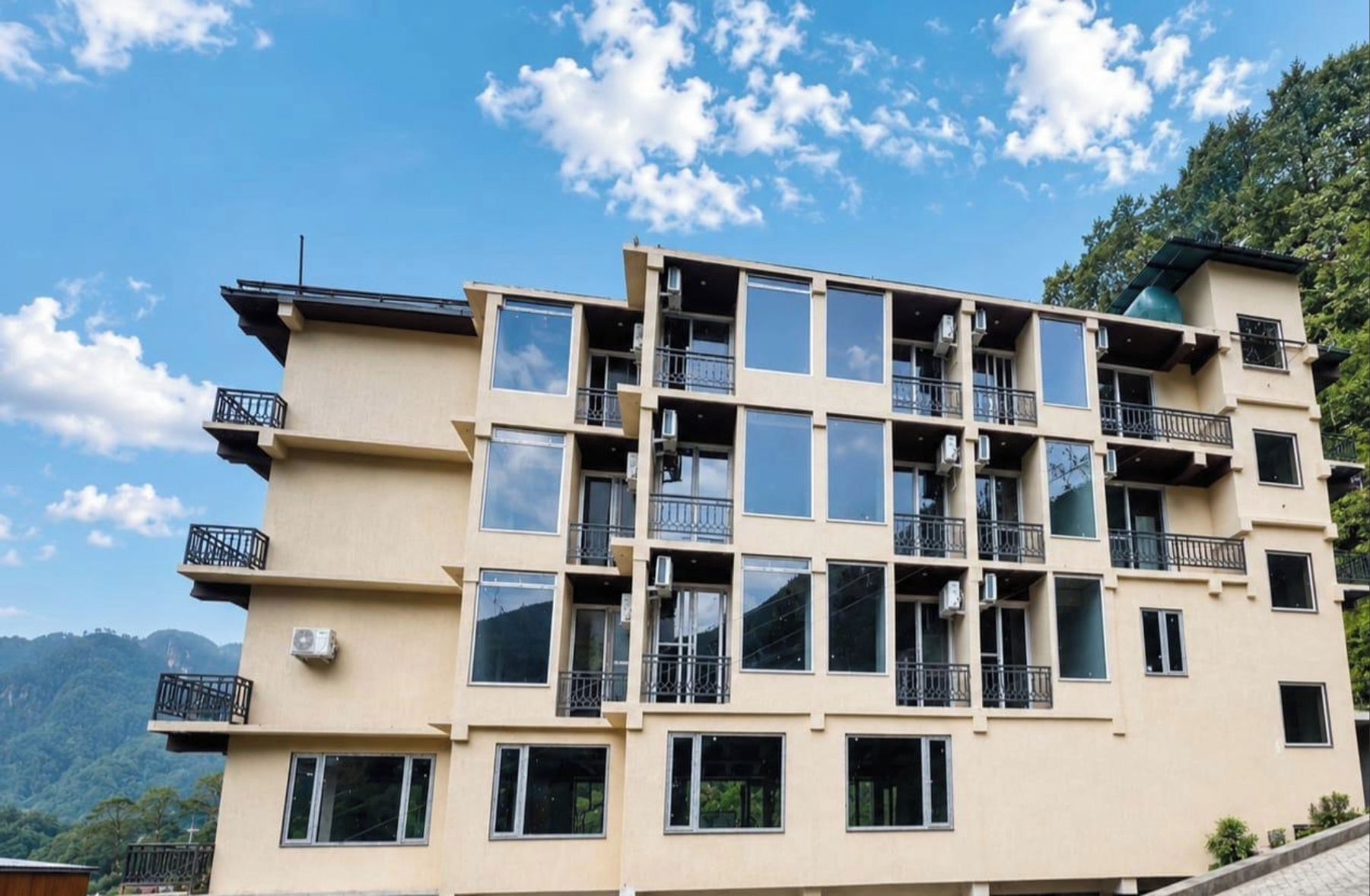 A multi-story building with balconies, large windows, and a mountainous backdrop.