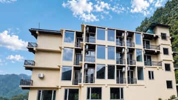 A multi-story building with balconies, large windows, and a mountainous backdrop.