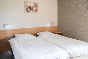Ein Hotelzimmer mit zwei Einzelbetten, einem Holzkopfteil, einer Ziegelwand und einem gerahmten Bild an der Wand.