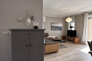 Ein modernes Wohnzimmer mit einem grauen Schrank, einer Couch, einem Fernseher und einer Pendelleuchte.