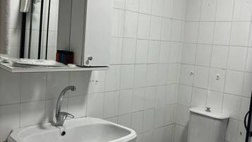 Casa de banho com lavatório branco, sanita e espelho sobre o lavatório.