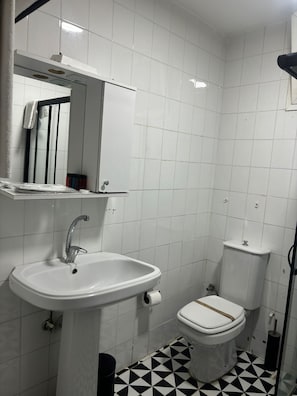 Casa de banho com lavatório branco, sanita e espelho sobre o lavatório.