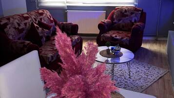 Una sala de estar con un sofá, una mesa de centro y un florero con flores rosadas.