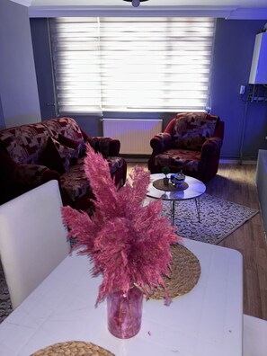 A living room with a sofa set, a coffee table, and a vase with pink flowers. - Pendik Carsi Merkezi Daire (Istanbul)