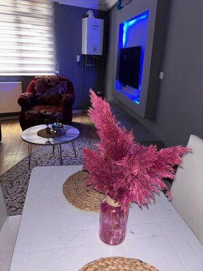 A living room with a white sofa, a coffee table, a decorative vase with pink foliage, a red armchair, and a wall-mounted TV with blue backlighting. - Pendik Carsi Merkezi Daire (Istanbul)