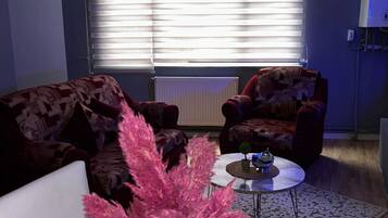 Uma sala de estar com sofá, poltrona, mesa de centro e plantas decorativas.
