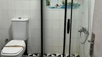 Un baño con inodoro, ducha con puerta de vidrio y suelo de baldosas.
