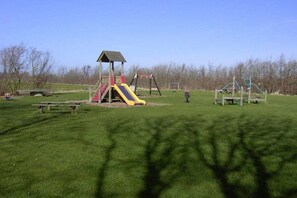 Une aire de jeux avec un toboggan, des balançoires et un petit abri.