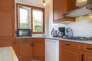 A kitchen with wooden cabinets, a microwave, a coffee maker, and a dishwasher. - De Golbreker Type 1AC (Zoutelande)