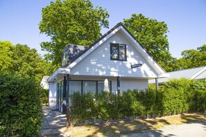 A white two-story house with a gabled roof, a covered porch, and a small garden area. - De Golbreker Type 1AC (Zoutelande)