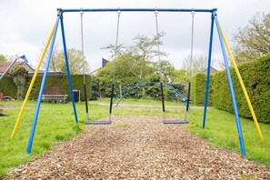 A swing set with a metal frame and chains, surrounded by a grassy area with a mulch ground cover. - The Golf Breaker - Type 1 (Zoutelande)