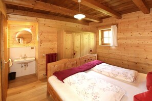 A wooden cabin bedroom with a bed, a window, a mirror, and a sink. - Pifrailerhof "Alte Mühle" (Schnals - Südtirol)