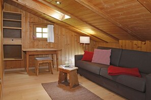 A cozy cabin interior with a wooden ceiling, a sofa with red cushions, a small table with a cup, and a window with a white curtain. - Pifrailerhof "Alte Mühle" (Schnals - Südtirol)