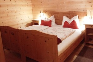 A wooden bed with a headboard, two bedside tables, and red and white pillows. - Pifrailerhof "Alte Mühle" (Schnals - Südtirol)