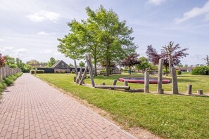 Un camí pavimentat que condueix a una zona verda amb arbres i un parc infantil.