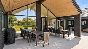 Eine Terrassengruppe im Freien mit Holztisch und -stühlen, einem Grill und Blick auf einen Garten.