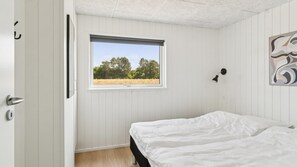 Ein Schlafzimmer mit einem Einzelbett, einem Fenster mit Blick auf ein Feld und Bäume sowie einer Wandlampe.