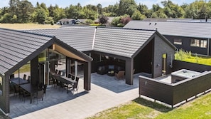 Un edificio moderno con una veranda coperta, una vasca idromassaggio e una zona pranzo con posti a sedere all'aperto.