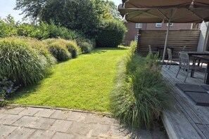 A well-maintained garden with a lawn, hedges, and a wooden deck with outdoor furniture. - Holiday home in Cadzand with swimming pool (Cadzand)