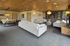 A modern interior with a wooden ceiling, a dining area with a table and chairs, and a seating area with sofas and a coffee table. - Holiday home in Cadzand with swimming pool (Cadzand)
