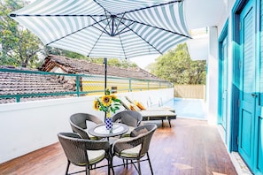 Eine Terrasse mit Tisch und Stühlen, einem gestreiften Sonnenschirm und Blick auf ein Schwimmbad.