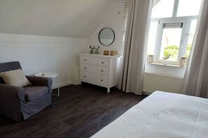A bedroom with a bed, a dresser, a chair, and a window with curtains. - Holiday home "Zee Gras" (Kamperland)