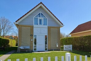 A two-story house with a front door, a small porch, and a white picket fence. - Holiday home "Zee Gras" (Kamperland)