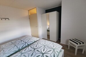 Een slaapkamer met een bed, een kledingkast en een klein krukje.
