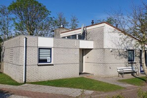 Een gebouw met twee verdiepingen, een bakstenen gevel, een duidelijke deur en een bankje buiten.