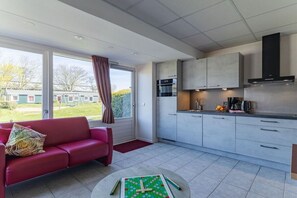 Eine moderne Küche mit weißen Schränken, einer schwarzen Dunstabzugshaube und einem Essbereich mit einem roten Sofa und einem Tisch mit einem Gesellschaftsspiel.