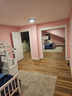 Ein Zimmer mit rosafarbenen Wänden, einem Etagenbett, einer weißen Tür und einem Holzboden.