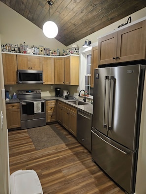 Una cocina con gabinetes de madera, un refrigerador de acero inoxidable, un microondas, un horno y una cafetera.