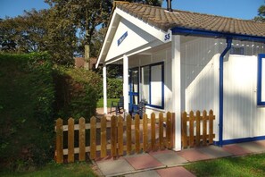 A small, single-story building with a white exterior and blue trim, number 33, featuring a porch with chairs and a wooden fence. - Holiday apartment in Zoutelande with Wi-Fi (Zoutelande)