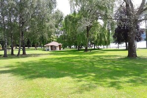 A park with a small building, trees, and a body of water in the background.