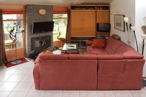 Een woonkamer met een hoekbank, een open haard, een televisie en een houten kast.