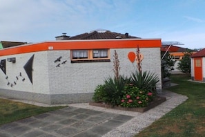 Een woongebouw met een witte gevel, oranje accenten en een kleine tuin met roze bloemen.